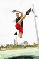 Mann beim Trampolin springen im Grünen vor Skyline