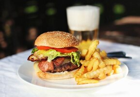 A hamburger with chips and beer on a table outside