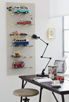 Shelves for toy cars on a wall with a desk and a retro lamp in front of them