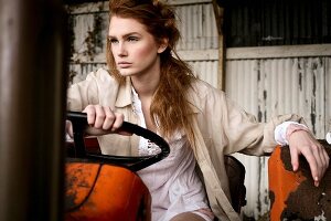 A young woman wearing a white blouse and a beige shirt on an old tractor