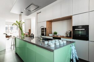 A white fitted kitchen with wooden details and an extractor hood above a mint-coloured kitchen island