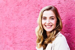 A portrait of a dark blonde woman against a pink wall