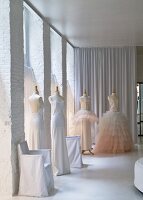 Schneiderpuppen mit weissen, eleganten Kleidern in geweisseltem Loftraum, im Hintergrund bodenlanger Vorhang
