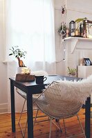 White fur blanket on retro chair at small black table below window