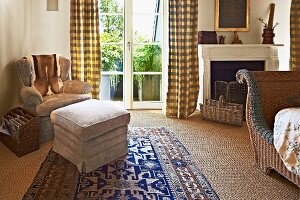 Footstool and armchair in corner of bedroom next to terrace doors with floor-length curtains