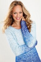 A blonde woman wearing a blue-toned, coarse-knit jumper with her hand on her neck