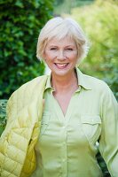 An older woman wearing a light green blouse and a quilted jacket in a garden