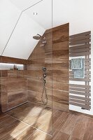 A walk-in shower with an illuminated shelf with wooden-style tiles and a towel radiator with open panels