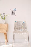 A classic bucket chair decoupaged with newspaper standing next to a wooden Scandinavian chest of drawers