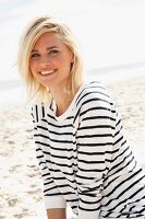 A blonde woman on a beach wearing a black-and-white striped, long-sleeved T-shirt