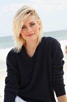 A blonde woman on a beach wearing a dark woollen jumper