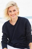 A blonde woman on a beach wearing a dark woollen jumper