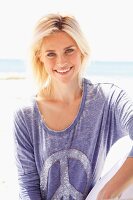 A blonde woman on a beach wearing a purple oil washed T-shirt with a peace symbol