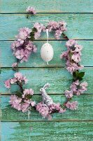 Wreath of pink cherry blossom with Easter egg and silver Easter bunny on wooden wall