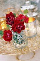 Rote Rosen und Lewisia in Glasvase mit Windlichtern auf einem Tortenständer