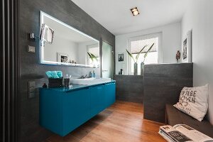 A contemporary bathroom with a petrol-coloured washstand under a mirror with grey tiles on a wall and a partition wall