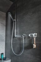 A grey-tiled shower cabin with taps and a hand-held shower head in a holder