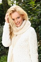 A young woman wearing a white, coarse-knit cardigan and scarf