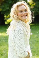 A young woman wearing a white, coarse-knit cardigan and scarf