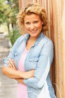 A blonde woman wearing a denim shirt leaning on a fence