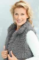 A blonde woman wearing a grey, faux fur gilet