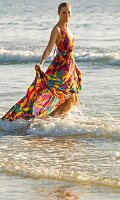 A blonde woman standing in the shallows of the sea wearing a colourful summer dress