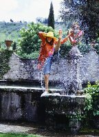 A young woman by a fountain wearing a transparent shirt and jeans