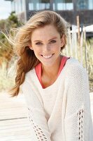 A young woman on a beach wearing a pink top and white knitted jumper