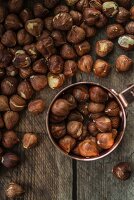 Hazelnuts in a copper cup and on a wooden surface