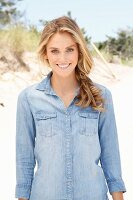 A young blonde woman on a beach wearing a denim shirt