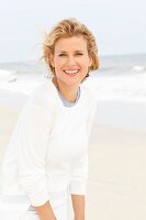 Blonde Frau in blauem Shirt und weißem Rundhalspulli am Strand