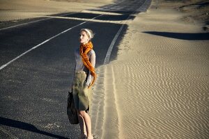 A blonde woman wearing an orange scarf, a grey shirt and a safari skirt
