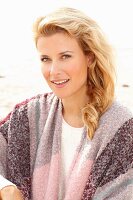 A blonde woman on a beach wearing a pink-toned shawl over her shoulders