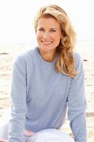 Blonde Frau mit blauem Pulli am Strand