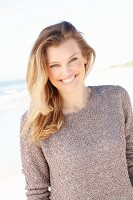 A young woman on a beach wearing a taupe jumper