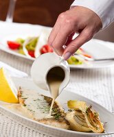 Sauce being poured over a fish fillet