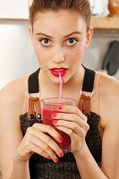 Young woman wearing top and dungarees drinking red smoothie