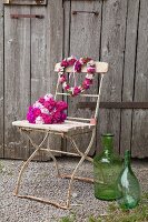 Bartnelkenstrauss und herzförmiger Blütenkranz auf Vintage Klappstuhl vor rustikalem Scheuenentor