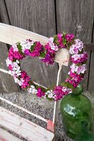 Heart-shaped wreath of Sweet Williams hung on backrest of vintage folding chair