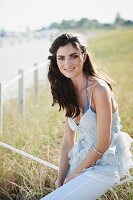 A dark haired woman wearing white trousers and a ruffled vest top