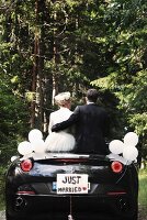 A bride and groom sitting in a convertible with a 'Just Married' sign