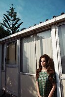A young woman wearing a patterned top leaning against a mobile home