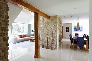 Open-plan interior with pale polished stone floor, lounge area, dining area with central fireplace in stone chimney breast