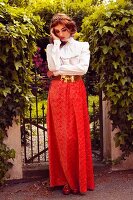 A young woman in a garden wearing a ruffled blouse and a long skirt