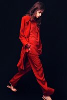 A young woman wearing a widely cut red trouser suit and a jacket