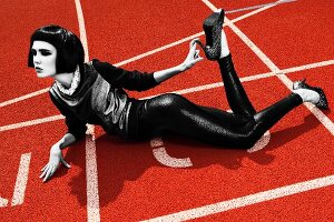 A young woman wearing a shiny top and leggings lying on a running track