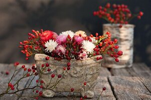 Herbstliches Blumengesteck mit Hagebutten in Steinschale auf Holztisch