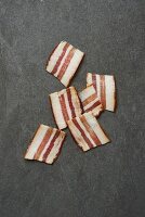 Six rashers of smoky bacon on a grey surface (seen from above)