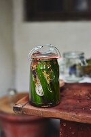 A jar of homemade gherkins with spices on a table