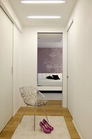White, feminine dressing room with fitted wardrobes, elegant metal chair and view into simple bedroom